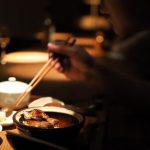 台北巷弄居酒屋的深夜用餐場景：昏黃溫暖的燈光下，食客正在木質吧台前享用剛出爐的手作熱食，呈現溫馨且放鬆的都市深夜煙火氣。